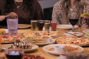 two women at table with feast of pizza, beer, wine, and sides on table